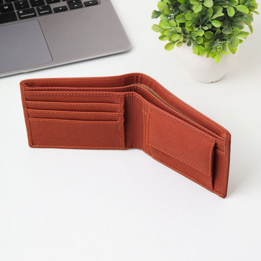 Open brown leather bifold wallet on a white desk beside a laptop for travel