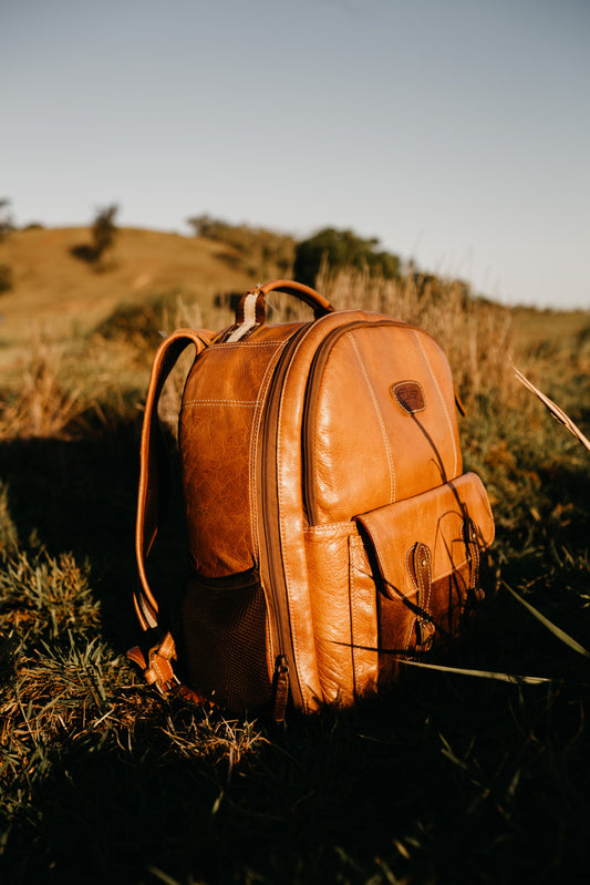 Brown vintage leather backpack resting on green grass field, outdoor lifestyle photography