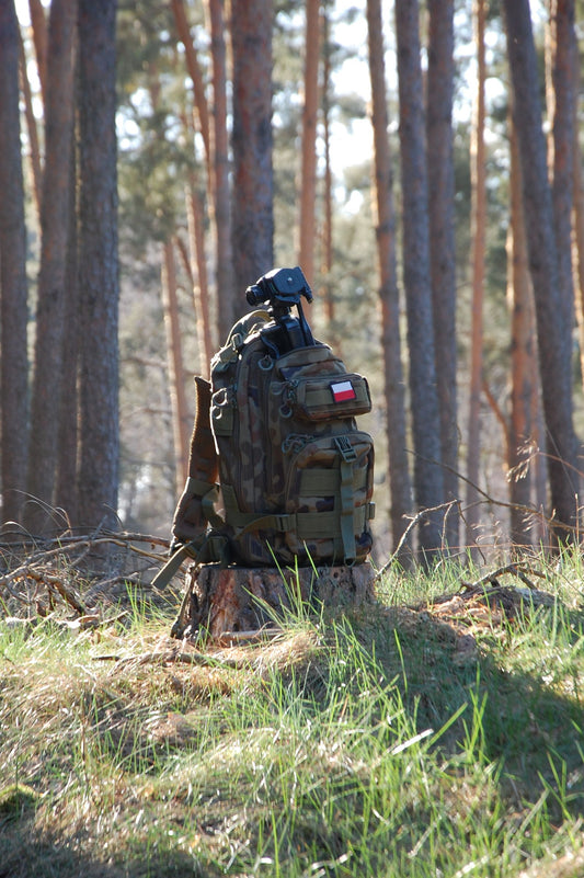 Tactical camouflage backpack with gear straps in a pine forest for outdoor adventures