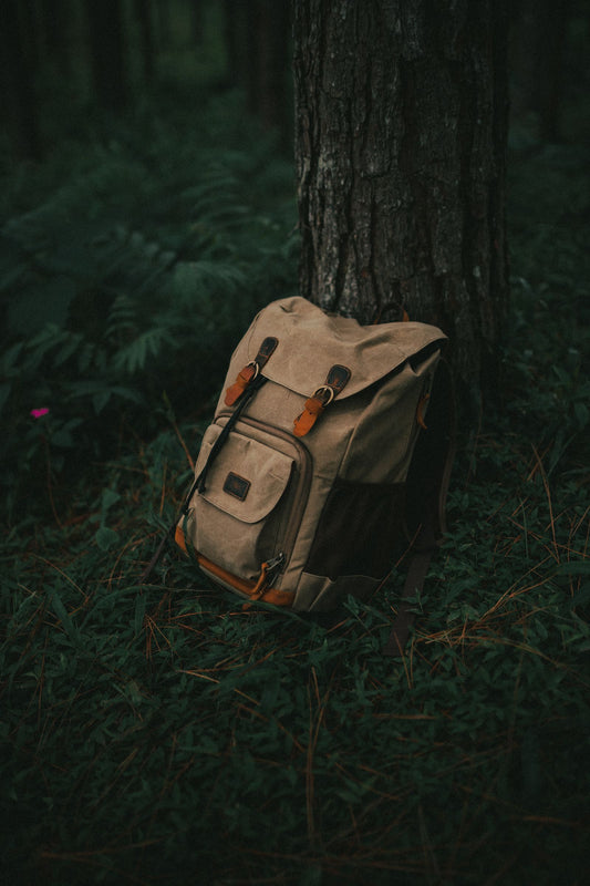 Waxed canvas backpack leaning against a forest tree, built for waterproof durability